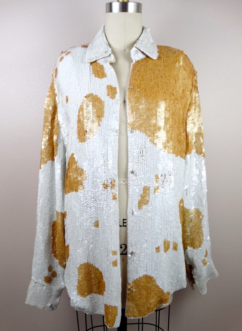 May include: A white and gold sequined button-up shirt with a long sleeve and a collared neckline.