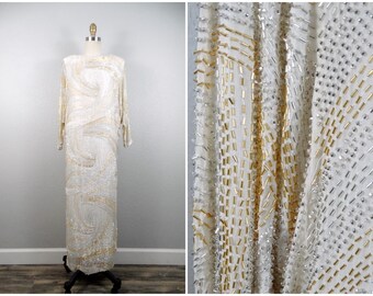 May include: A white maxi dress with gold and silver beading. The dress has a swirling pattern and is made of a sheer fabric.