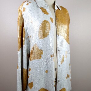 May include: A long-sleeved sequined shirt with a white background and gold sequin accents. The shirt has a button-up front and a relaxed fit.
