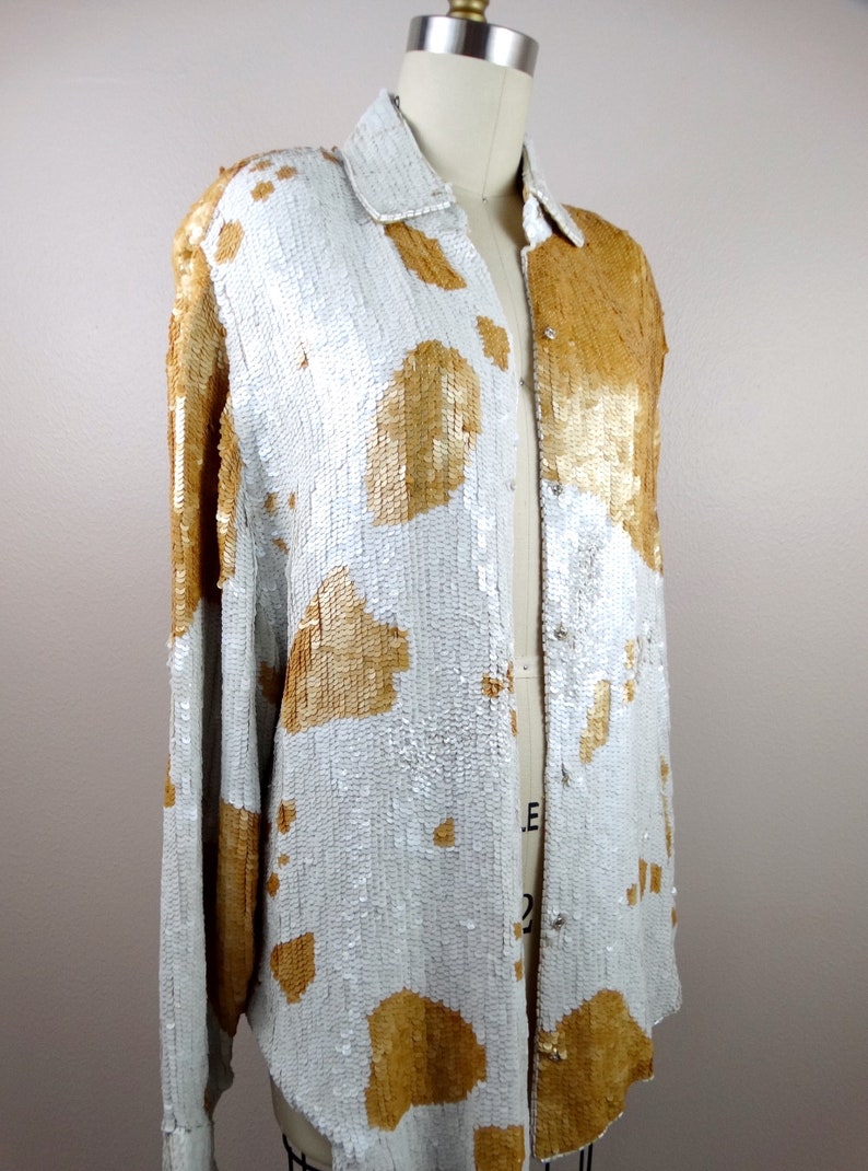 May include: A long-sleeved sequined shirt with a white background and gold sequin accents. The shirt has a button-up front and a relaxed fit.