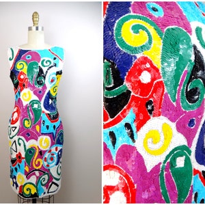 May include: A sleeveless white dress with a colorful abstract pattern made of sequins. The pattern includes swirls, circles, and geometric shapes in shades of pink, blue, green, yellow, red, and black.