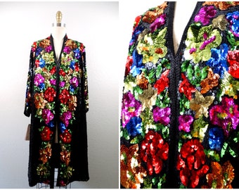 Könnte beinhalten: Eine lange schwarze Jacke mit Pailletten und einem Blumendesign in Rot-, Grün-, Blau-, Rosa- und Goldtönen. Die Jacke hat einen V-Ausschnitt und lange Ärmel.