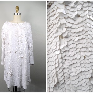 Peut inclure: Une robe blanche en sequins. Les sequins sont disposés en forme d'écailles.