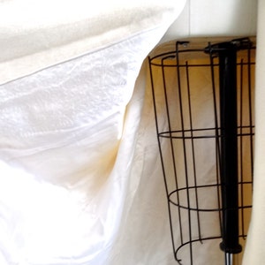 May include: A white fabric draped over a black metal stand with a round base. The stand has a vertical metal rod extending from the base.