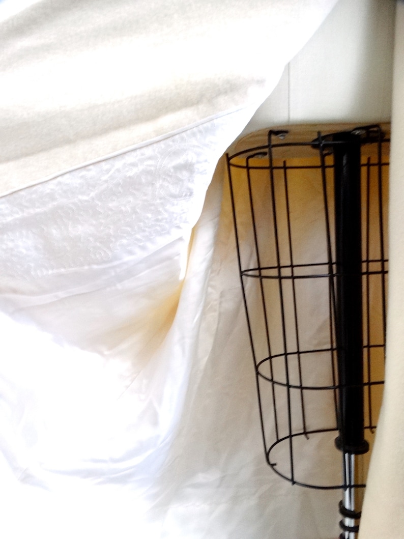 May include: A white fabric draped over a black metal stand with a round base. The stand has a vertical metal rod extending from the base.