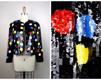 May include: A black sequined jacket with colourful polka dots. The dots are red, yellow, blue, and white. The jacket has a  "COLLAPSIBLE SHOULDER" label and the number "2" on the front.