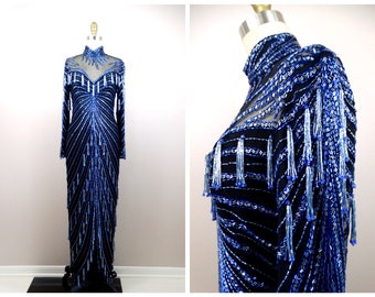 May include: A long, blue and black beaded evening gown with a high neck and long sleeves. The gown is covered in sequins and beads, and has a fringe detail on the shoulders and down the sides.