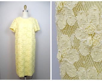 Puede incluir: Un vestido amarillo de encaje con un patrón floral y detalles de cuentas. El vestido tiene mangas cortas y un escote redondo.