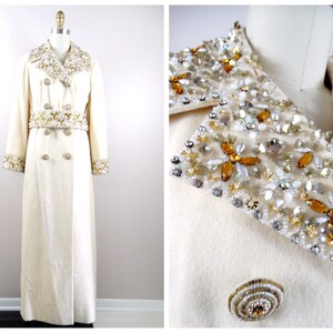 May include: A long white coat with a double breasted closure and a large embellished collar and belt. The embellishments are made of gold, silver, and clear beads.