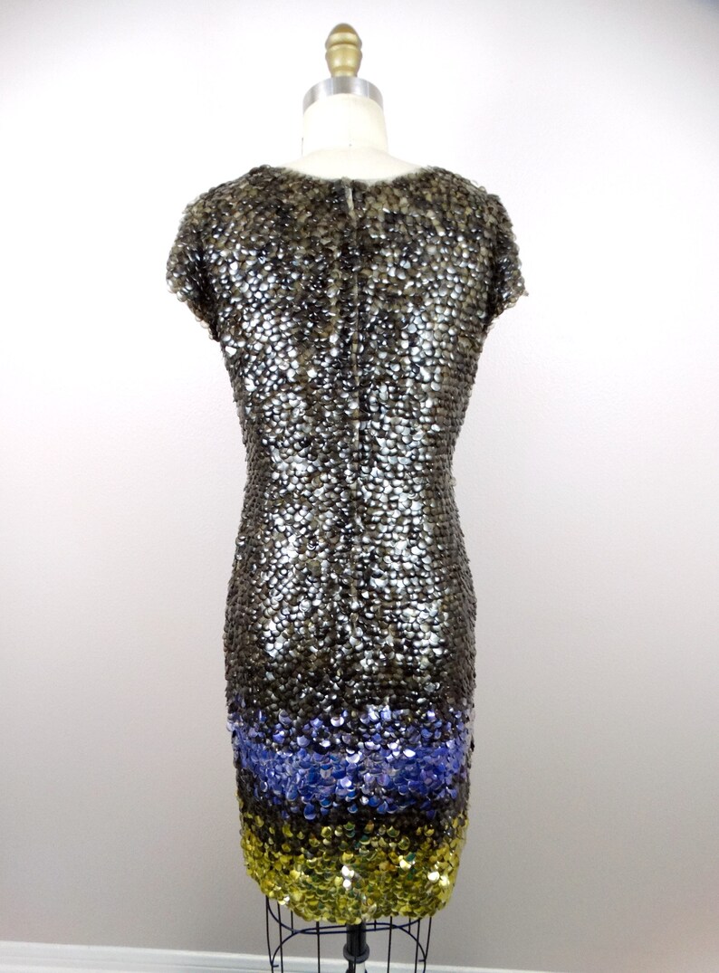 May include: A short-sleeved sequined dress with a gradient design. The top of the dress is a dark grey colour, transitioning to a light blue colour, and then to a gold colour at the bottom.