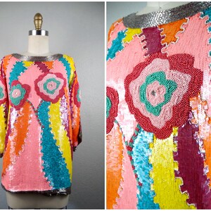 May include: A colorful sequined top with a floral design. The top features a patchwork design with pink, orange, yellow, and blue sequins. The neckline and cuffs are trimmed with silver sequins. The floral design is made of red and green beads.