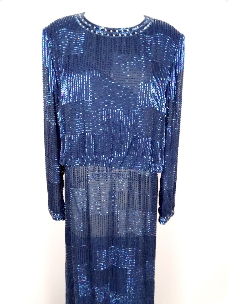 May include: A long-sleeved, navy blue dress with a geometric pattern made of iridescent sequins. The dress has a round neckline and a fitted silhouette.