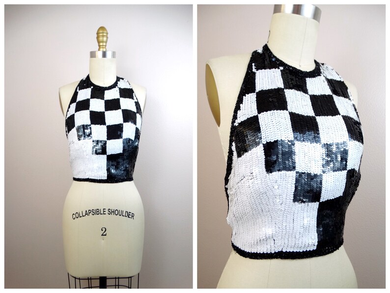 May include: Black and white checkered halter top made of sequins. The top is cropped and has a halter neckline. The top is on a white mannequin.