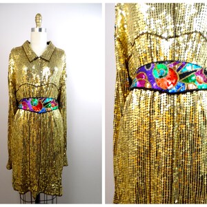 Può includere: Un abito di paillettes dorate con maniche lunghe e collo a camicia. L'abito ha una cintura ricamata colorata con un motivo geometrico.