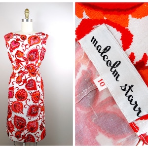 Puede incluir: Un vestido blanco sin mangas con estampado floral rojo y naranja. El vestido tiene una silueta ajustada y un escote redondo. El vestido está etiquetado como "Malcolm Starr" y talla 10.