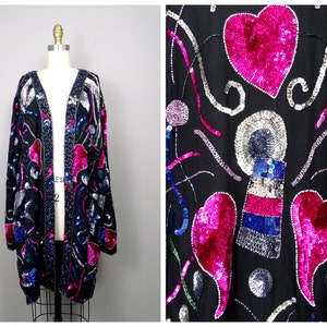 Puede incluir: Una chaqueta negra de lentejuelas con cuello en V y mangas largas. La chaqueta está decorada con lentejuelas de colores en una variedad de formas, incluyendo corazones, círculos y remolinos. La chaqueta es una pieza llamativa que sería perfecta para una noche fuera.