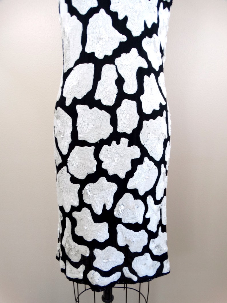 May include: A black and white sequined dress with a cow print pattern. The dress is sleeveless and has a fitted silhouette.