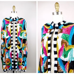 Könnte beinhalten: Eine bunte Paillettenjacke mit einem schwarz-weißen Streifenbesatz. Die Jacke hat ein geometrisches Muster in den Farben Pink, Blau, Grün und Gold.