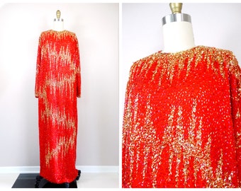 Könnte beinhalten: Ein langes rotes Paillettenkleid mit goldenen Akzenten. Das Kleid hat einen runden Ausschnitt und lange Ärmel. Die Pailletten sind in einem Muster angeordnet, das an Wellen erinnert.
