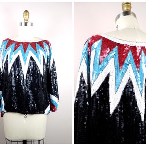 Puede incluir: Una blusa negra de lentejuelas con un patrón geométrico en blanco, rojo y azul. El patrón es una serie de zigzags.