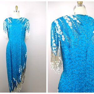 May include: A turquoise sequined dress with white beaded fringe detailing. The dress has a fitted bodice and a flowing skirt.