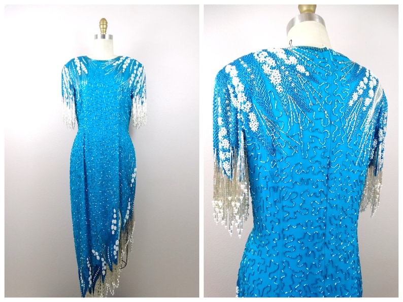 May include: A turquoise sequined dress with white beaded fringe detailing. The dress has a fitted bodice and a flowing skirt.