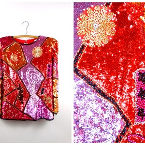 May include: A red, pink, and orange sequined top with a geometric pattern. The top has long sleeves and a round neckline.