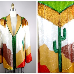 May include: A white sequined jacket with a desert landscape design. The jacket features a green cactus, brown mountains, and gold sequins. The jacket has a green zipper and a gold fringe collar.
