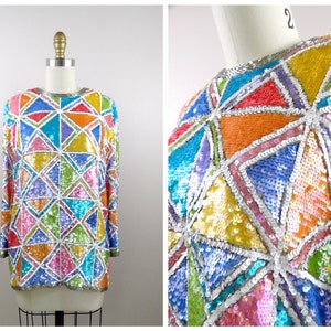 May include: A colorful sequined top with a geometric pattern in shades of blue, green, pink, orange, and yellow. The top has long sleeves and a round neckline.