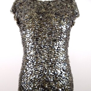 May include: A silver sequined dress with a round neckline and short sleeves. The dress is made of small, overlapping sequins that create a shimmering effect.
