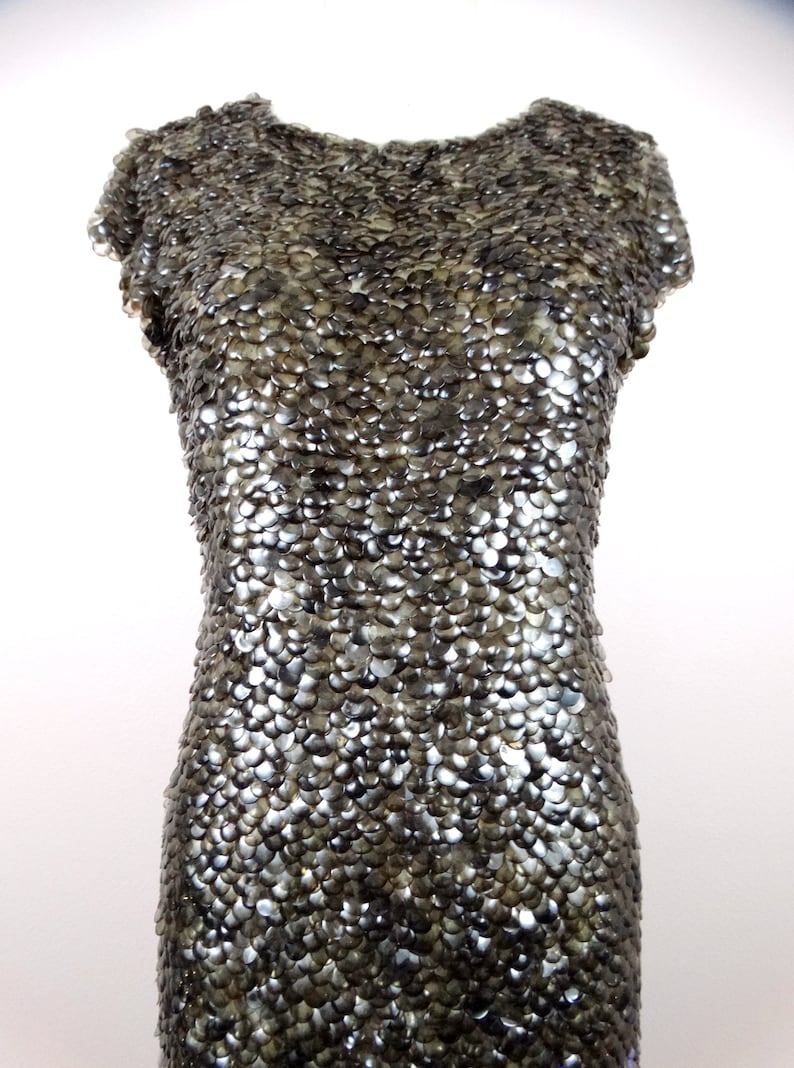 May include: A silver sequined dress with a round neckline and short sleeves. The dress is made of small, overlapping sequins that create a shimmering effect.