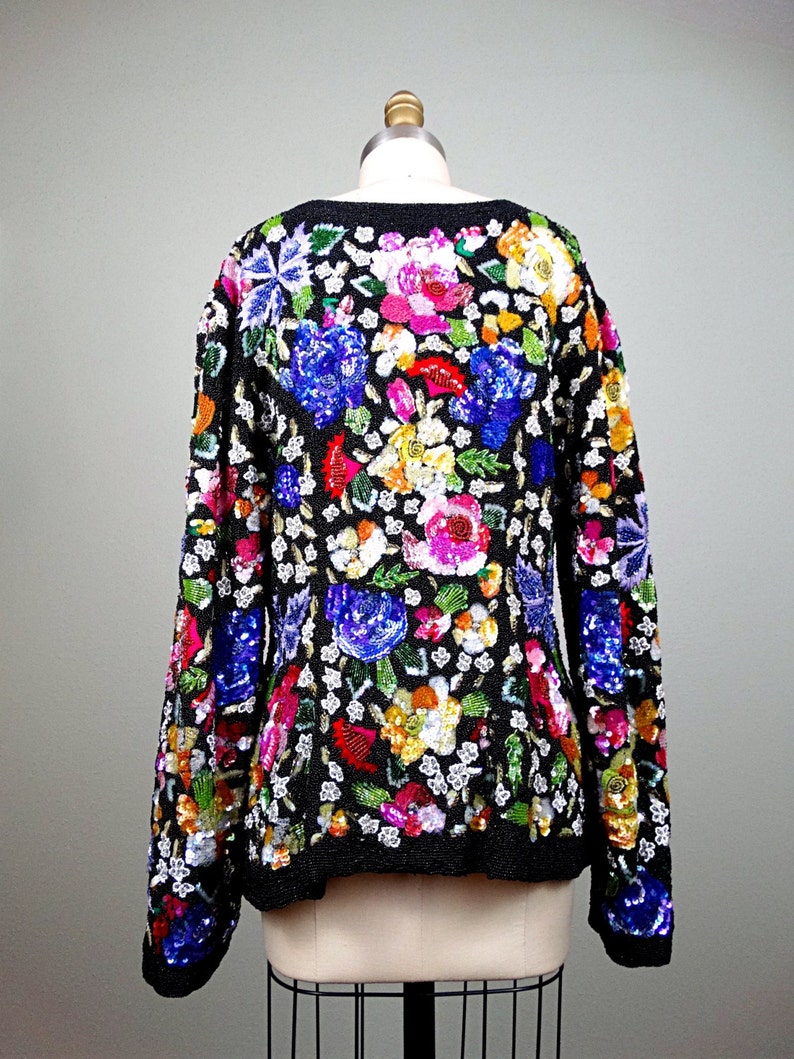 Pode incluir: Um su&eacute;ter preto de manga comprida com um padr&atilde;o floral feito de lantejoulas. As lantejoulas s&atilde;o de v&aacute;rias cores, incluindo rosa, azul, verde, amarelo e laranja.