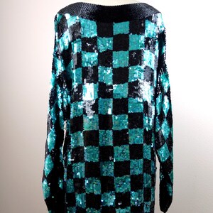 Puede incluir: Una blusa de lentejuelas azul verdoso y negro con un patr&oacute;n de cuadros. La blusa tiene mangas largas y un cuello de barco.