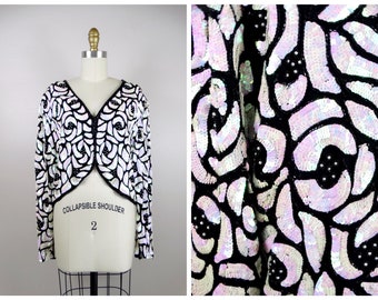 May include: A black and white sequined jacket with a cropped, collared design. The jacket has a zipper closure and a 'Collapsible Shoulder' label on the front.