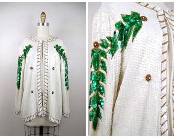 May include: A white sequined jacket with green and gold leaf embroidery. The jacket has a long sleeve and a button closure.
