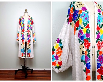 May include: White sequined kimono with colorful floral embroidery. The embroidery features a variety of flowers in shades of red, orange, yellow, green, blue, and purple.