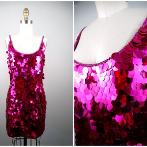May include: A fuchsia sequin mini dress with thin straps. The dress is displayed on a mannequin, showcasing its shimmering, scale-like texture. The sequins create a gradient effect, transitioning from a lighter pink at the top to a deeper magenta at the bottom.