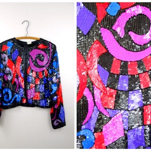 May include: A black sequined jacket with a colorful geometric pattern in shades of red, pink, blue, and purple. The jacket has a zipper closure and long sleeves.