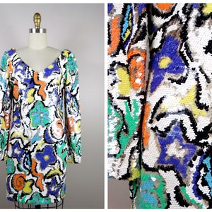 Puede incluir: Un vestido blanco mini con un patrón abstracto colorido hecho de lentejuelas. El patrón incluye azul, verde, naranja, amarillo y negro.