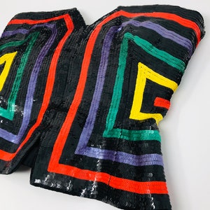 May include: A black sequined top with colourful geometric stripes in red, yellow, green, and purple.
