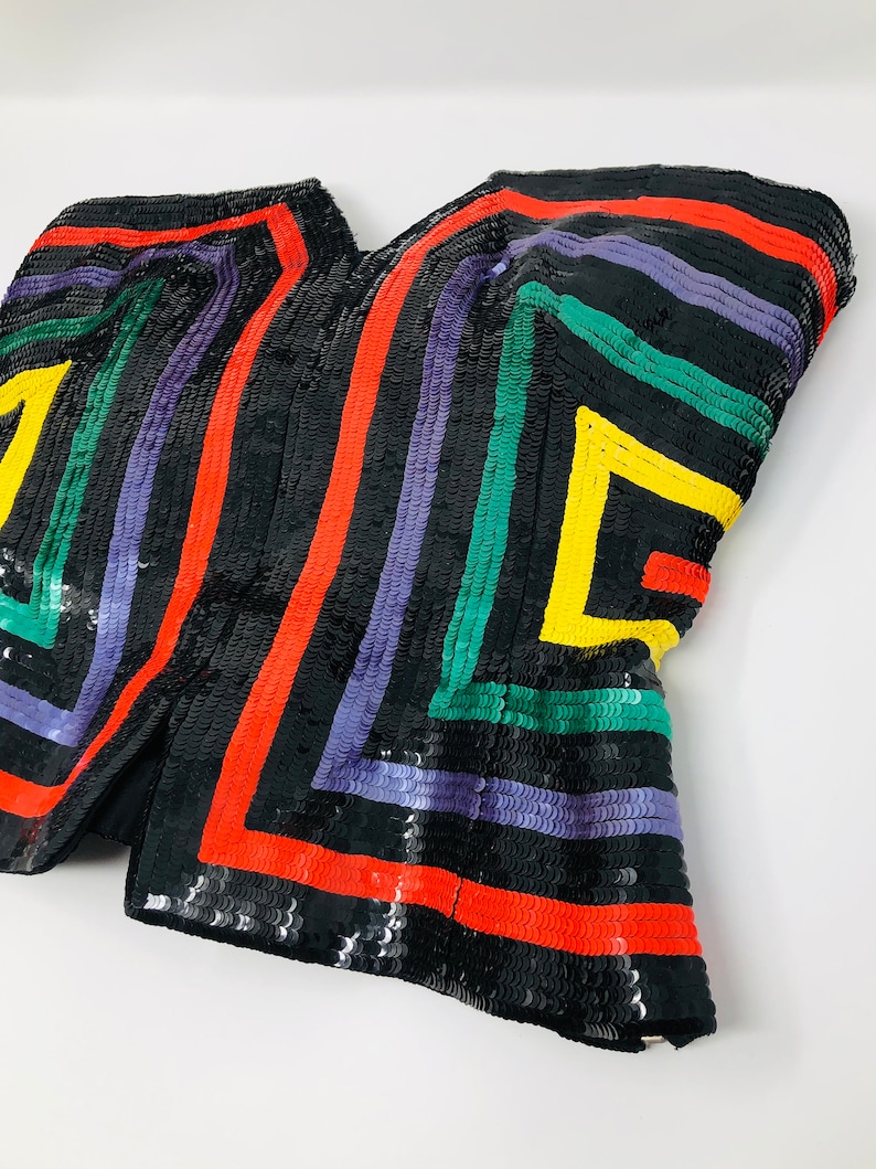 May include: A black sequined top with colourful geometric stripes in red, yellow, green, and purple.