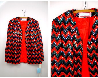 May include: A red sequined jacket with a black and green chevron pattern. The jacket has a  'SOMETHING! Dress Up to Dress Down' label.