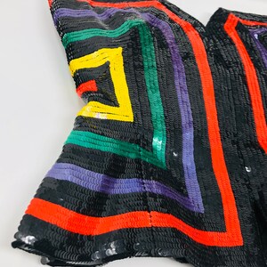 May include: A black fabric with colourful geometric patterns made from sequins. The fabric features red, green, yellow and purple sequins arranged in a geometric design.