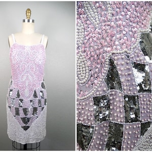 Peut inclure: Robe vintage, longueur genou, sur mannequin. La robe est ornée de sequins et de perles dans les tons de rose, d'argent et de blanc. Le corsage présente un motif complexe, tandis que la jupe a un motif à carreaux. La robe a de fines bretelles.