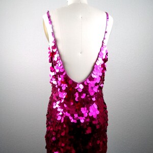 May include: A sleeveless, magenta sequin dress with a deep V-neck and spaghetti straps. The dress is displayed on a mannequin, showcasing its shimmering, eye-catching design. The sequins create a textured, glamorous look.