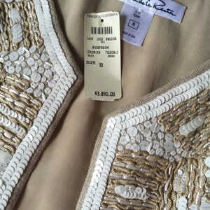 May include: A beige sleeveless vest with white sequins and embroidery. The vest has a label that reads "Oscar de la Renta" and "Bergdorf Goodman". The label also includes the size 10 and the price $3,890.00.