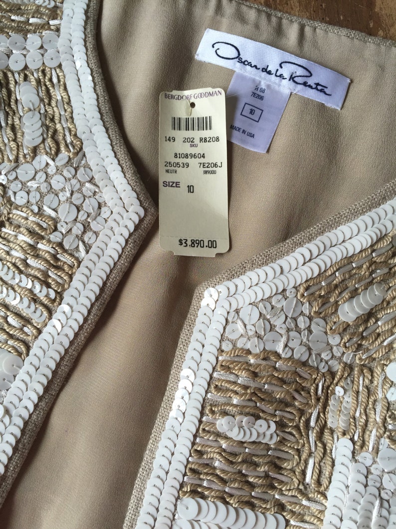 May include: A beige sleeveless vest with white sequins and embroidery. The vest has a label that reads "Oscar de la Renta" and "Bergdorf Goodman". The label also includes the size 10 and the price $3,890.00.