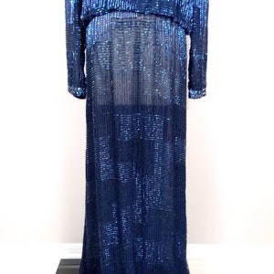 May include: A long, navy blue sequined dress with a fitted bodice and a flowing skirt. The dress is made of small, iridescent sequins that create a shimmering effect.