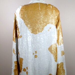 May include: A white and gold sequined shirt with a long sleeve and a button-up front.