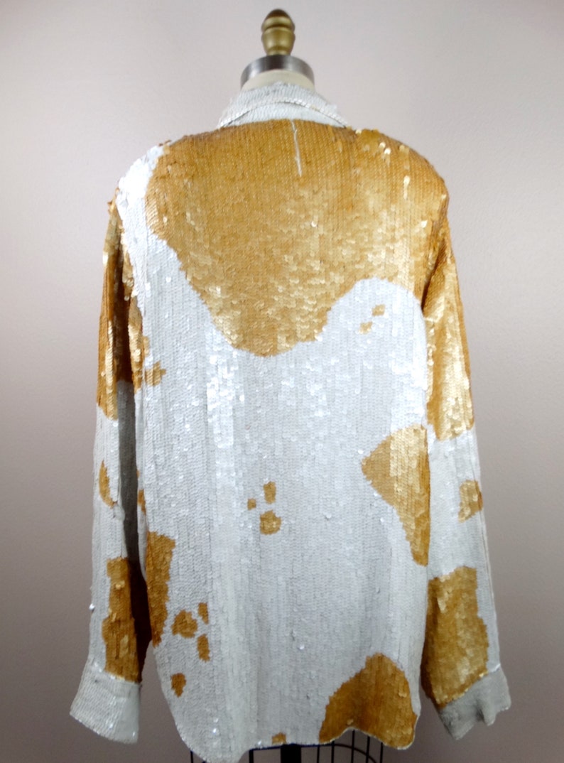 May include: A white and gold sequined shirt with a long sleeve and a button-up front.